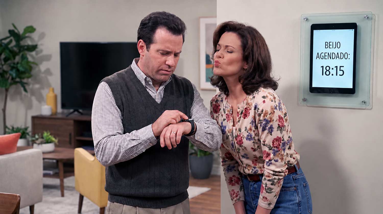A man is looking at his watch as his wife stands next to him with her lips puckered, waiting for their scheduled 6:15 pm kiss, as shown on their digital schedule on the wall.